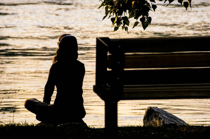 Photo by Toni Reed silhouette of person sitting on bench near body of water during daytime