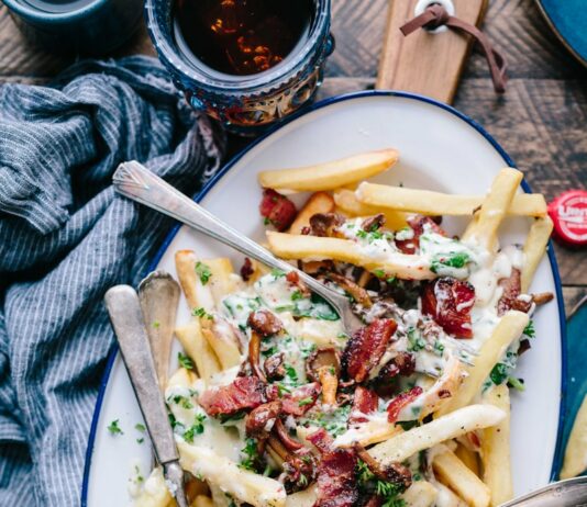 운동 전후에 좋은 음식과 피해야 할 음식 bacon strips and melted cheese topped fries on oval white and blue platter with gray stainless steel forks